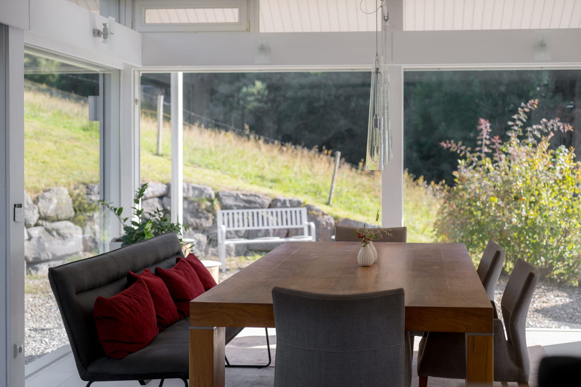 Long dining table at the glass front, the meadow behind it